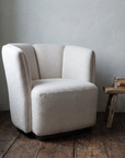 Single cream armchair in a cool grey plaster corner beside a wooden stool with books