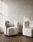 White armchairs in soft morning window light with a bare branch in a stoneware jug
