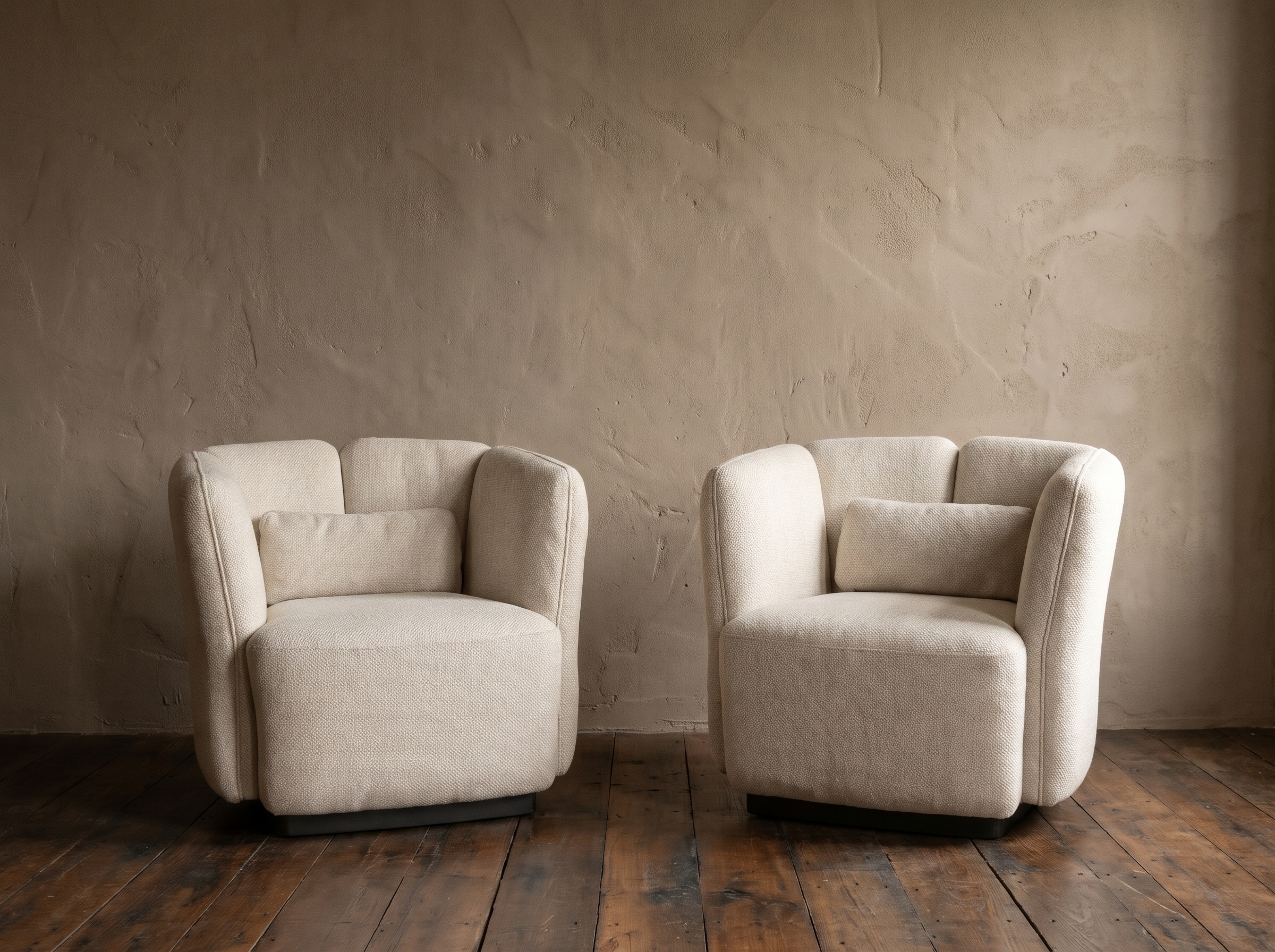 Pair of white textile Ford armchairs by Living Couture against a warm taupe plaster wall on dark reclaimed wood floor