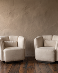 Two white Italian armchairs in a quiet plaster room with a light switch for scale