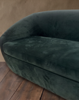 Detail of plush deep green velvet seat cushion and curved arm of a tub sofa