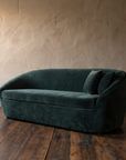Three-quarter view of a green velvet tub sofa showing its wraparound curved back and upholstered base