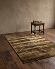 Olive and umber Ralph Lauren rug styled with an antique side table, old books and a cup of tea
