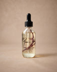 Hinoki + Lemongrass Aromatic Body Oil by Mum's Milk, glass dropper bottle with a dried botanical sprig