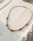Gold Art Nouveau scrolled necklace with five small faceted stones, laid flat on pale stone