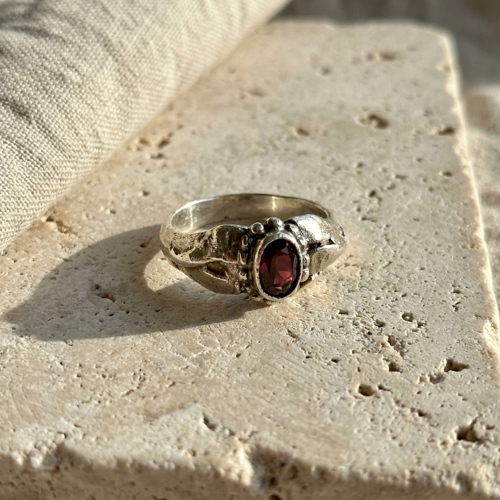 Sterling silver ring with a bezel set oval garnet, laid flat on pale stone