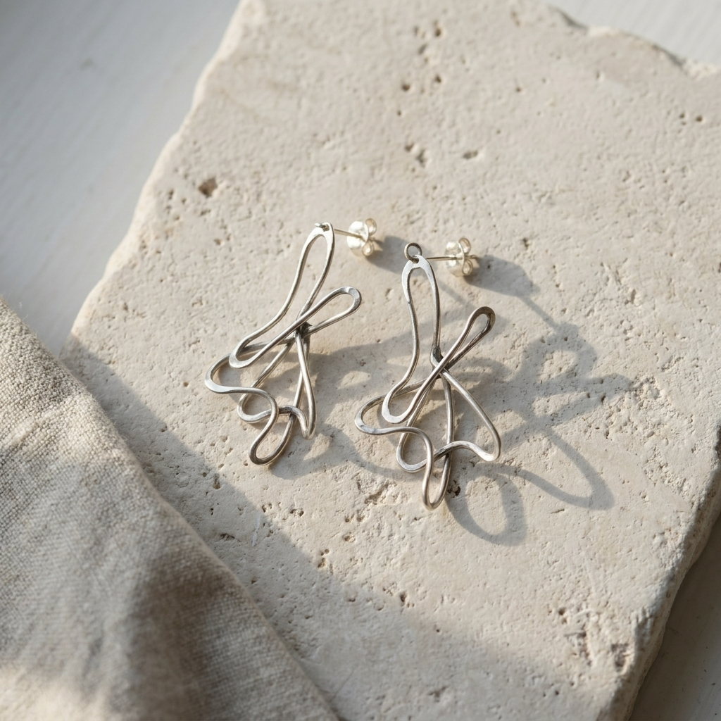 Hand formed sterling silver looped wire earrings, laid flat on pale stone