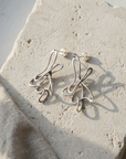 Hand formed sterling silver looped wire earrings, laid flat on pale stone