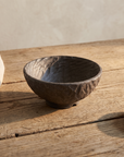 Large grey hand carved ceramic bowl on a weathered wood table in soft daylight