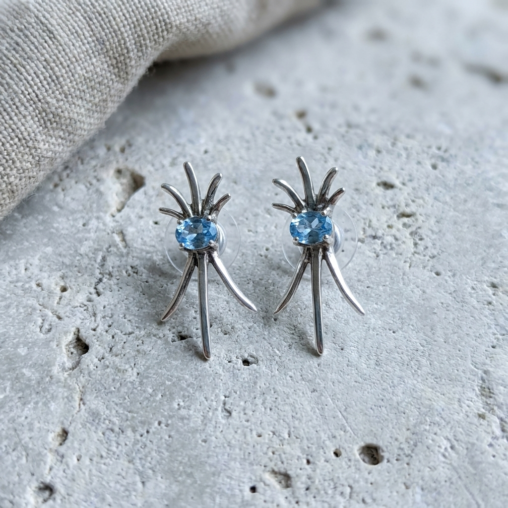 Sterling silver starburst earrings with blue topaz, laid flat on pale stone