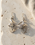 Twisted hammered sterling silver ribbon earrings with inner hanging loops, laid flat on pale stone