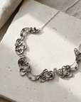 Art Nouveau oxidised sterling silver scroll collar set with garnets and peridots, laid flat on pale stone