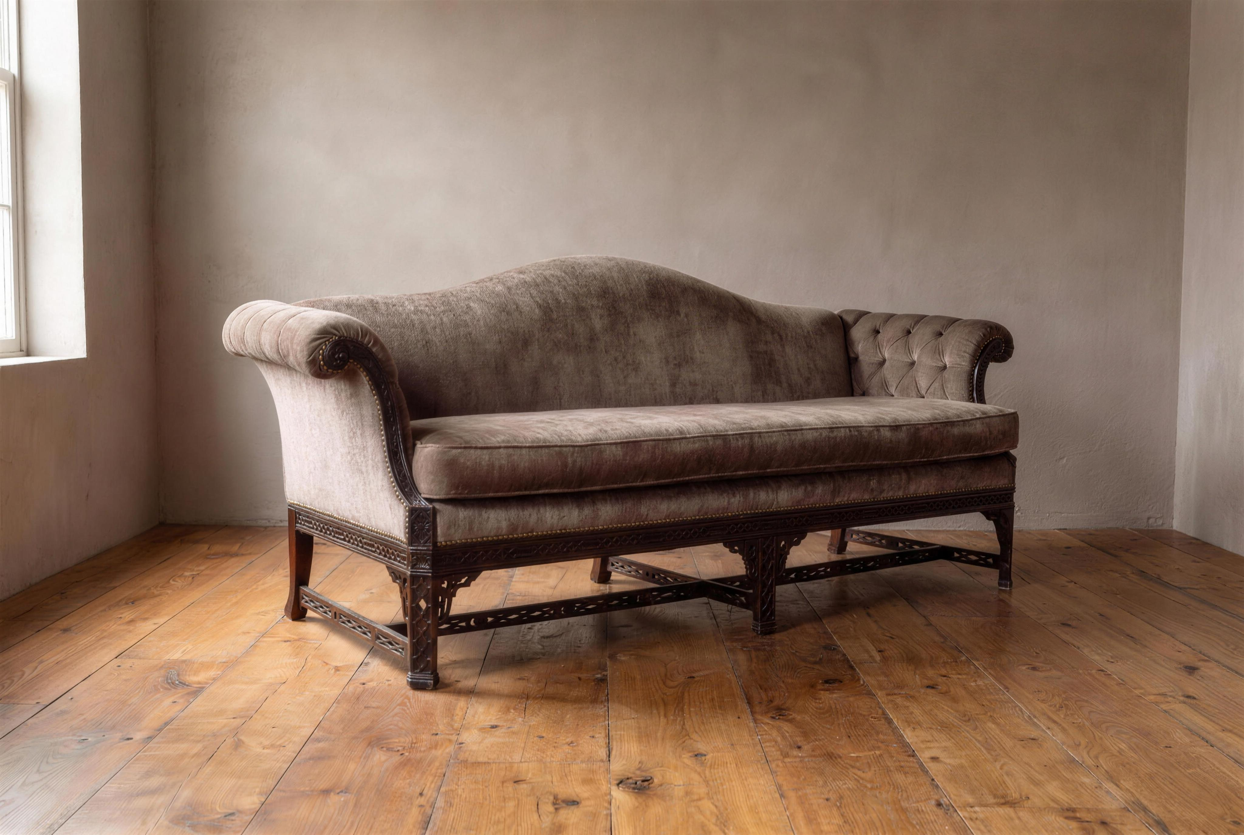 Three-quarter view of the camelback sofa showing the pleated scroll arm, tufted arm, fretwork legs and stretcher