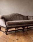 Three-quarter view of the camelback sofa showing the pleated scroll arm, tufted arm, fretwork legs and stretcher