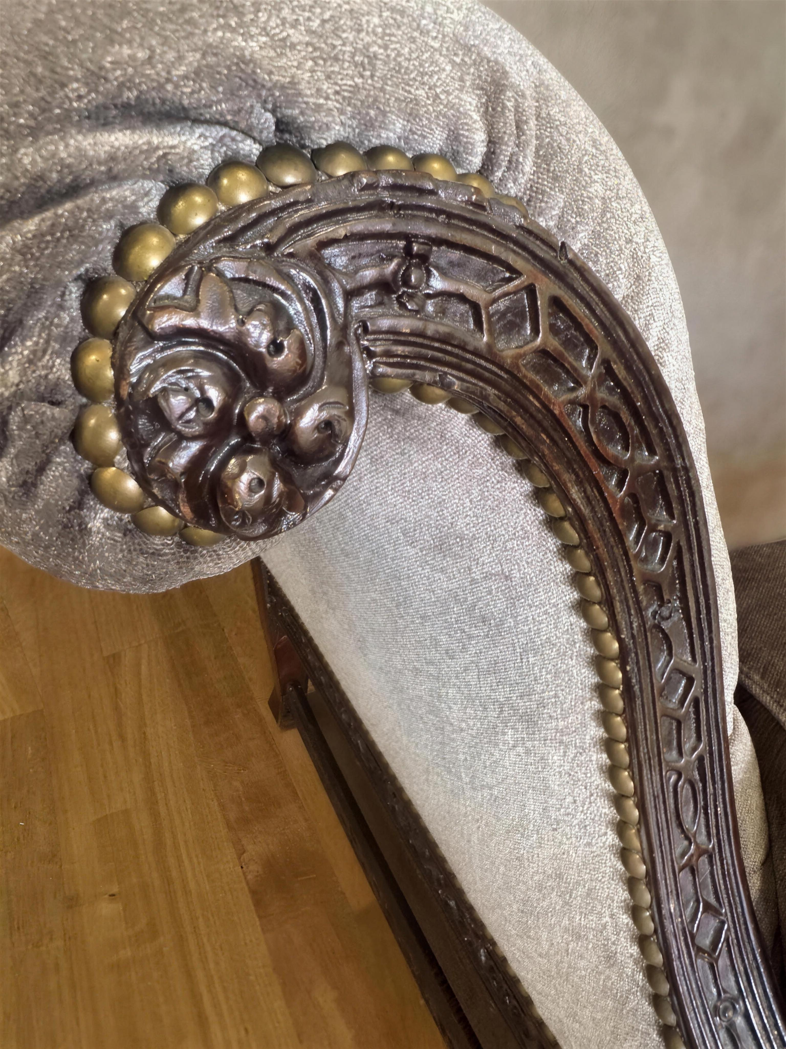 Close-up of the hand-carved leafy arm end ringed in large brass nailheads, with lattice fretwork facing