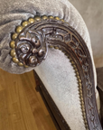 Close-up of the hand-carved leafy arm end ringed in large brass nailheads, with lattice fretwork facing