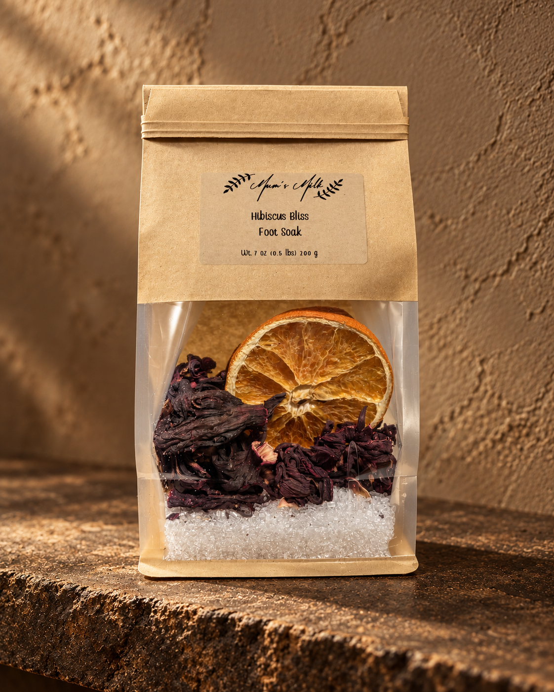 Mum's Milk Hibiscus Bliss Foot Soak pouch on weathered stone against warm taupe plaster