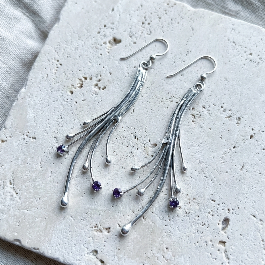 Long sterling silver comet earrings with fanned rods and small amethysts, laid flat on pale stone