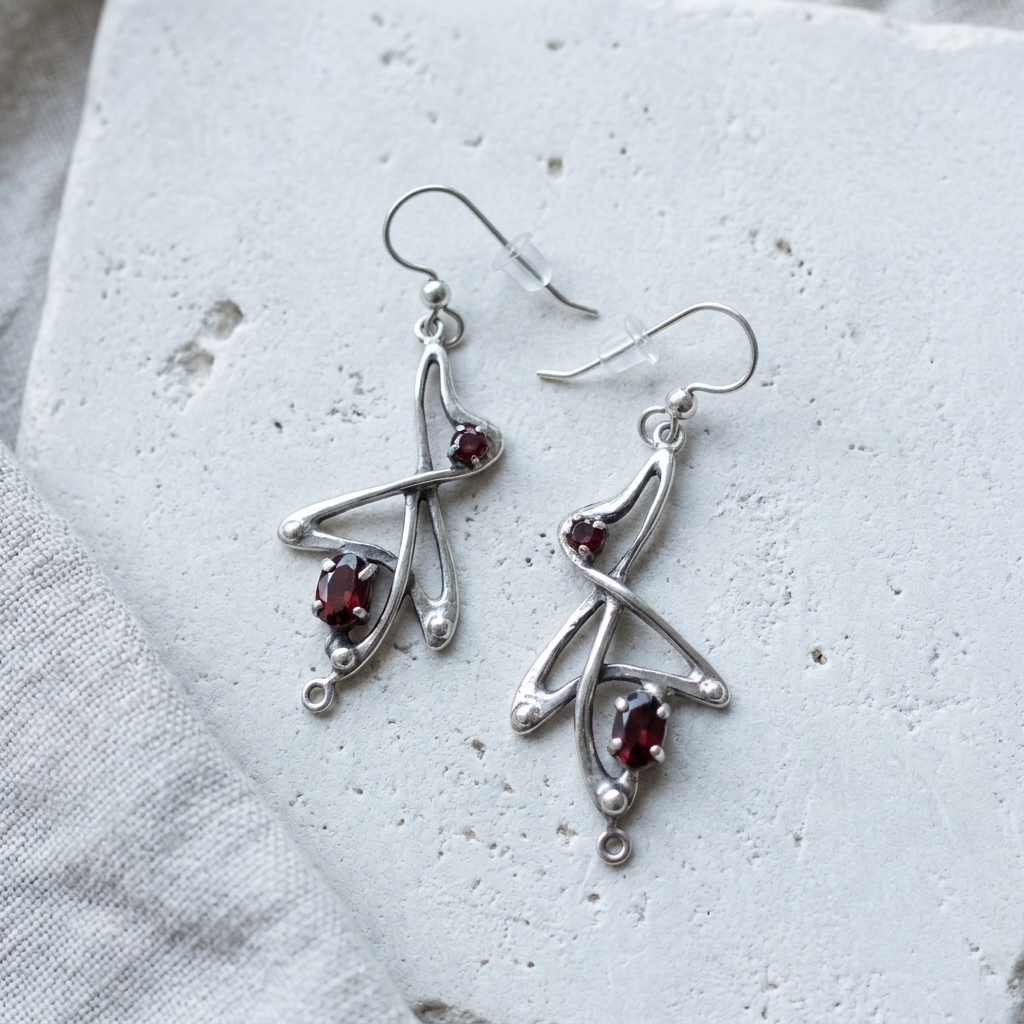 Angular sterling silver Art Nouveau drop earrings set with garnets, laid flat on pale stone