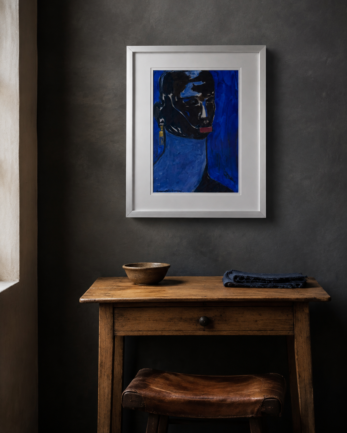 Framed blue portrait hung above a pine side table in a dark plaster room
