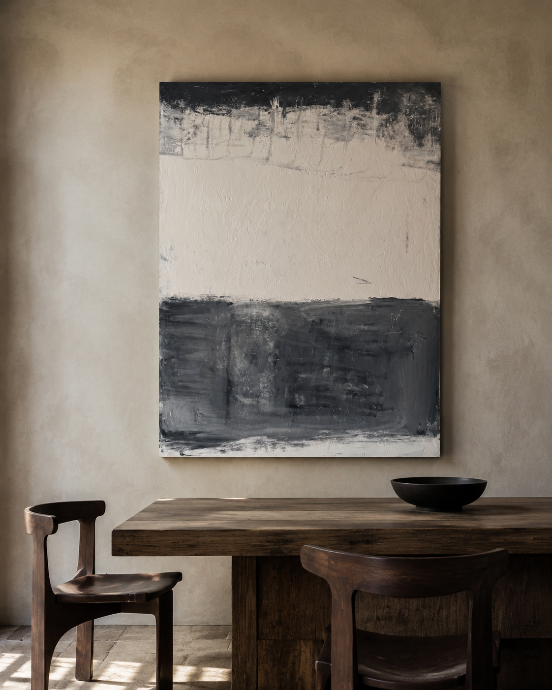 Black and bone abstract painting hung above a rustic dining table in a warm plaster room