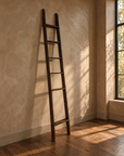 Full view of the tall weathered wood ladder leaning naturally against a plaster wall