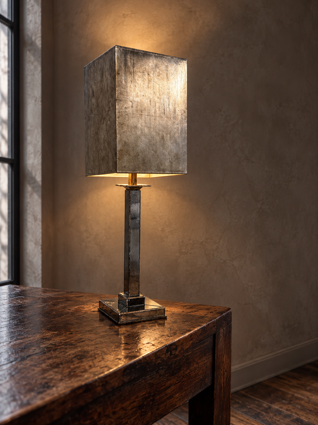 Mirrored column table lamp illuminated on a reclaimed wood console against taupe plaster