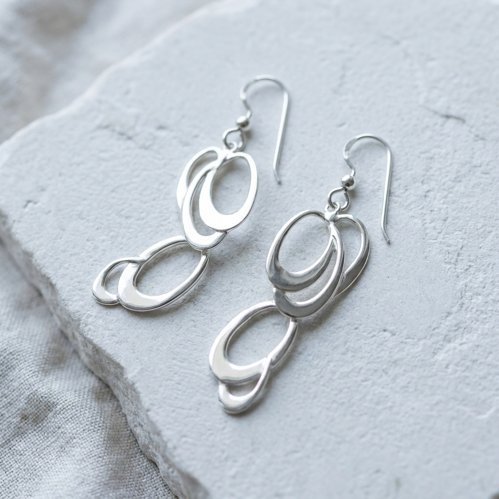 Polished sterling silver interlocking oval drop earrings laid flat on pale stone